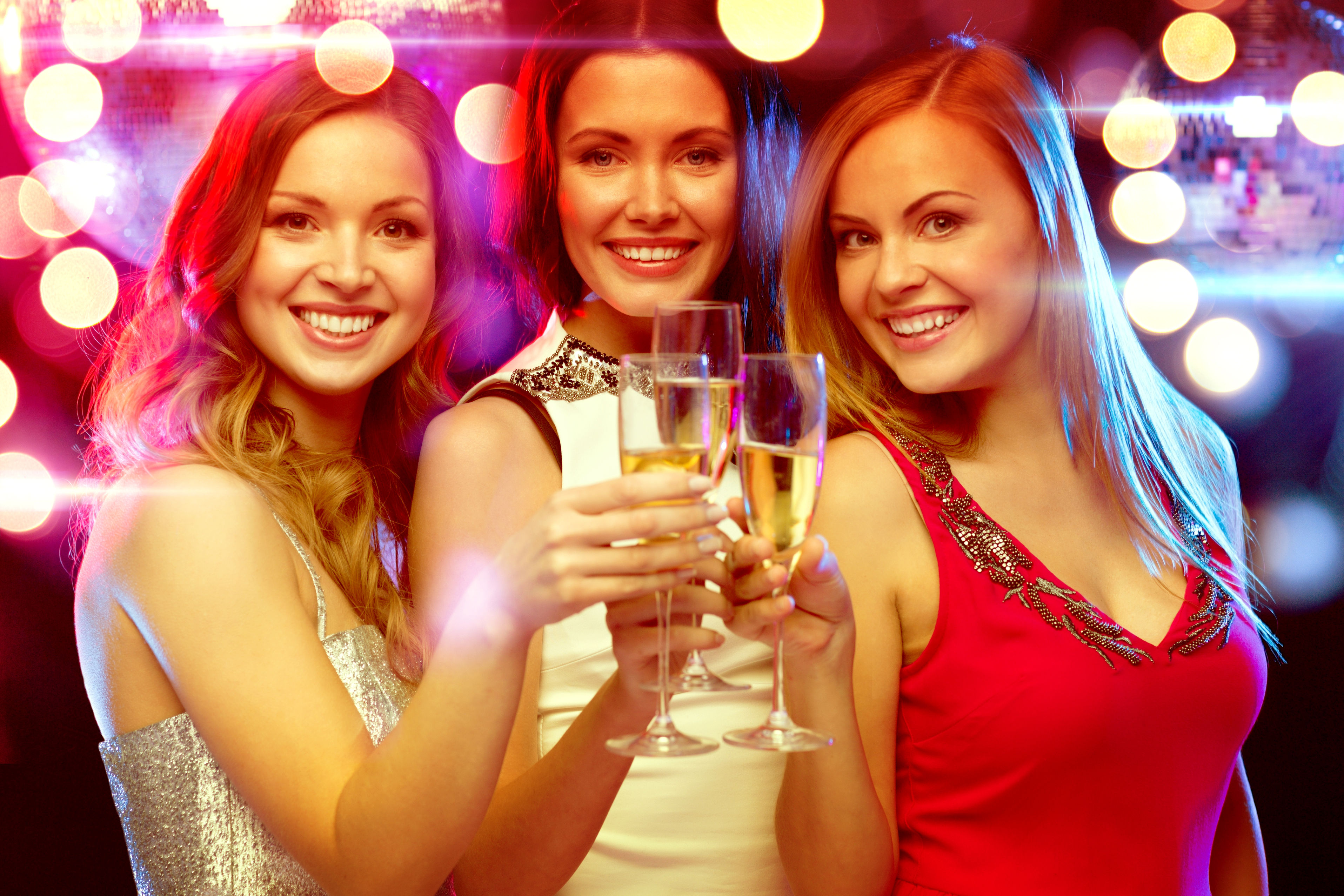 Three women holding champagne glasses in a party.